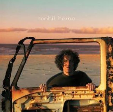 Oben steht "mohit home". Eine Person hält eine alte, rostige Autotür am Strand bei Sonnenuntergang.