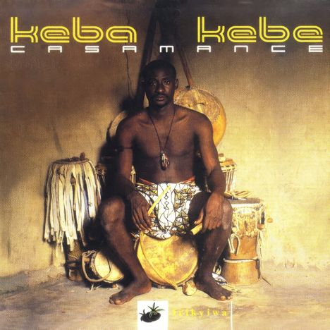 Text: "Keba Kaba Casamance", "jikyjwa". Ein Mann sitzt vor Trommeln, trägt ein traditionelles Tuch und ein Amulett.