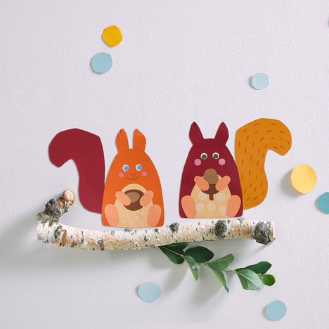 Zwei bunte, illustrierte Eichhörnchen sitzen auf einem Ast, umgeben von bunten Kreisen.