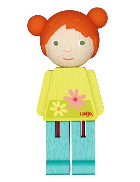 Logo "HABA" auf einem gelben Blumenrock, rote Haare, einfache Holzfigur mit blauen Beinen, fröhliches Design.