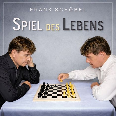 Text: "FRANK SCHÖBEL SPIEL DES LEBENS". Zwei Männer spielen Schach, einer in Schwarz, der andere in Weiß gekleidet.