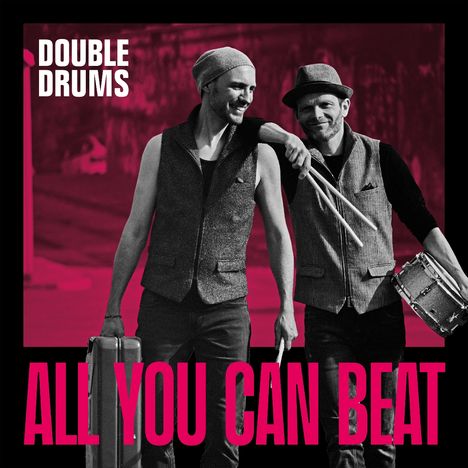 "DOUBLE DRUMS. ALL YOU CAN BEAT." Zwei lächelnde Männer in Westen, einer mit Trommelstöcken, der andere mit Koffer. Schwarz-weiß.
