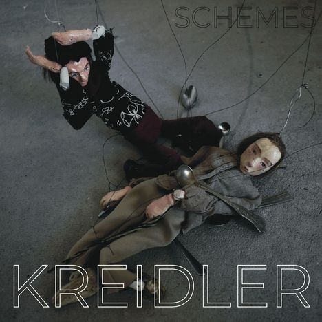 Text: „SCHEMES“ und „KREIDLER“. Zwei Puppen mit Drähten und Löffeln auf einem Boden liegend.