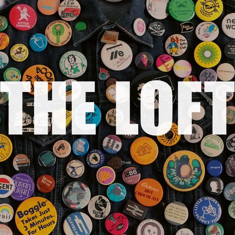 Große weiße Buchstaben "THE LOFT" über einer Sammlung bunter Buttons und Abzeichen auf einem Jeansstoff.