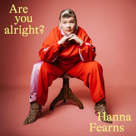 Text: "Are you alright?" Eine Person in rotem Trainingsanzug sitzt lässig auf einem Stuhl vor rosa Hintergrund.