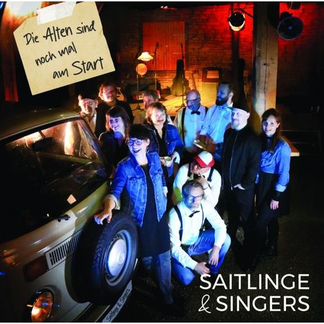 "Die Alten sind noch mal am Start." Eine Gruppe feiert fröhlich um einen alten Van, im Hintergrund Bühne mit Instrumenten.