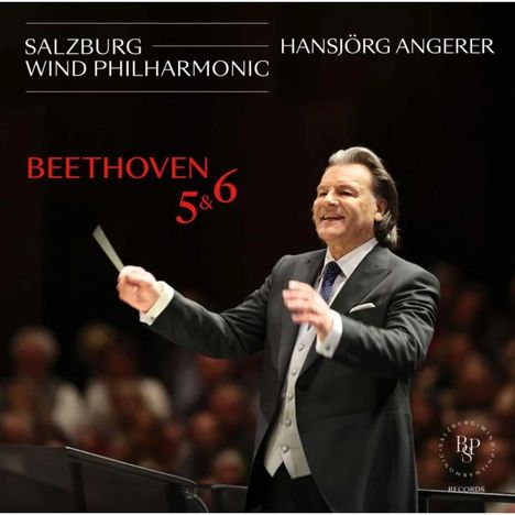 "Salzburg Wind Philharmonic, Hansjörg Angerer, Beethoven 5 & 6." Ein Dirigent in Aktion, lächelnd, mit erhobenem Taktstock.