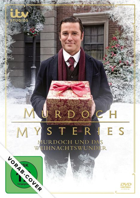 „MURDOCH MYSTERIES: MURDOCH UND DAS WEIHNACHTSWUNDER“, Mann in Anzug mit rotem Schal hält Geschenk, winterliche Szene.