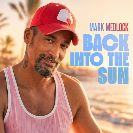 „MARK MEDLOCK BACK INTO THE SUN“. Ein Mann mit roter Kappe und rosa Tanktop lächelt am Strand bei Sonnenuntergang.