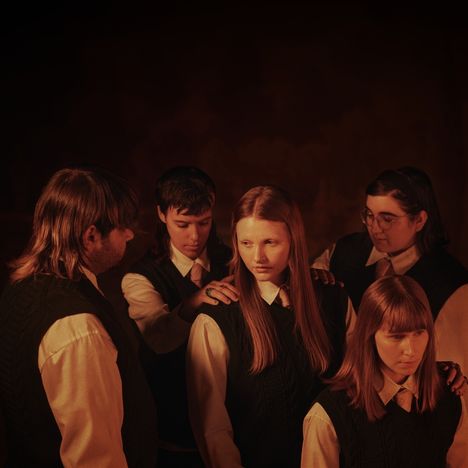 Fünf junge Menschen in Schuluniform, stehen in düsterem Licht. Eine legt die Hand auf eine andere Schulter.