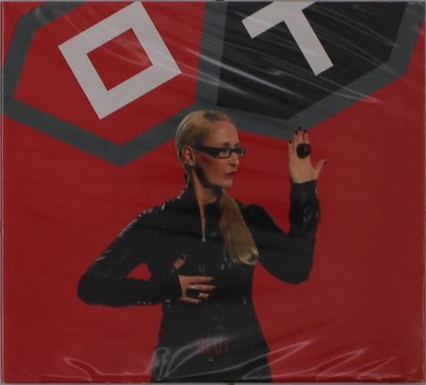 Text: "OT" und "BLUT". Eine Frau mit Brille und blondem Haar in schwarzem Outfit posiert vor rotem Hintergrund.
