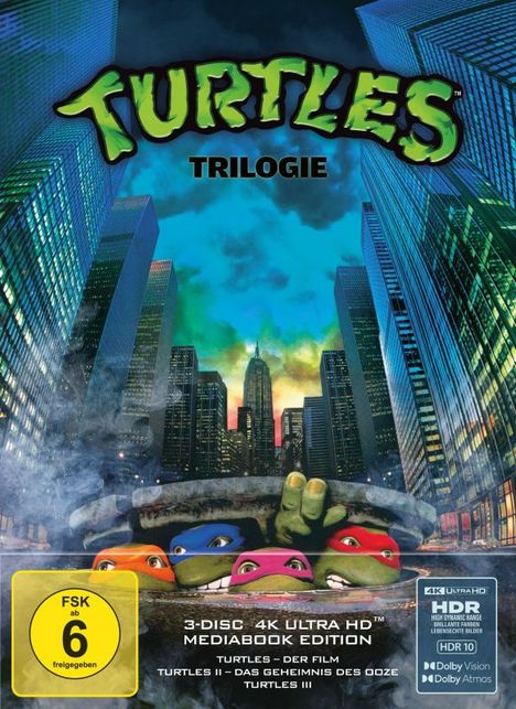 "Turtles Trilogie". Vier maskierte Schildkröten schauen aus einem Gullydeckel inmitten einer Stadt mit hohen Gebäuden.