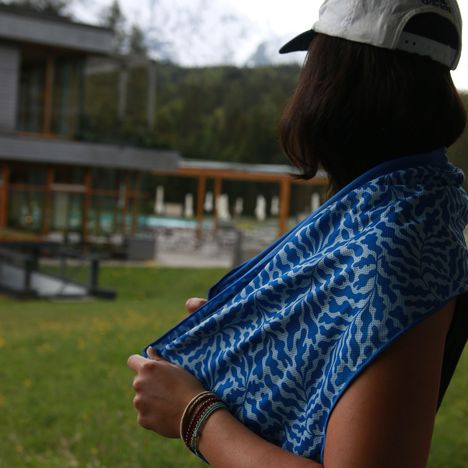 Eine Person im Profil trägt eine weiße Kappe, hält ein blau gemustertes Tuch. Im Hintergrund ein modernes Gebäude.