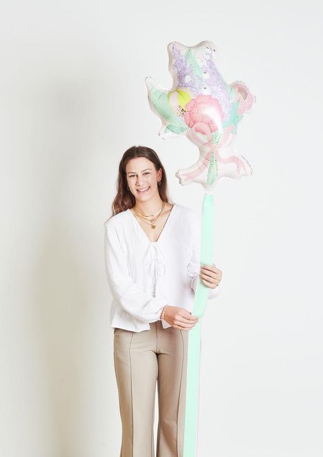 Eine lächelnde Person hält einen pastellfarbenen, sternförmigen Ballon mit floralen Mustern.
