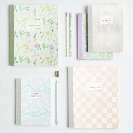 Notizbücher und Bleistifte mit floralen und geometrischen Mustern, sanfte Pastellfarben.