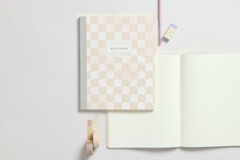 Notizbuch mit kariertem Cover und Text "LAY-FLAT BINDING", "BLANK PAGES", "NOTEBOOK", "BAMBOO PAPER". Nebenbei Stift und Radiergummi.