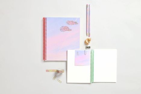 Notizbuch mit Wolken, daneben Stifte, Anspitzer, Klebeband, Büroklammern auf weißem Hintergrund.