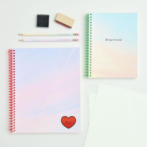 Zwei Notizbücher, eines mit "The Sky is the Limit", ein Stempel, zwei Bleistifte und ein herzförmiges rotes Gesicht.