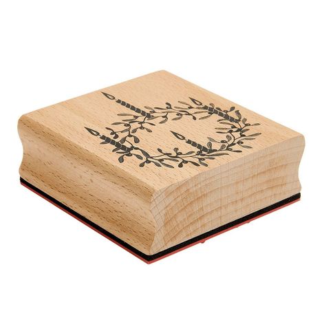 Ein Holzstempel mit einem schwarz gezeichneten Kranz aus Zweigen und Blättern auf der Oberfläche.
