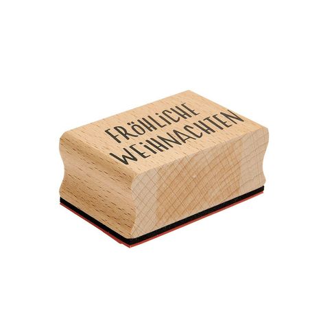 Ein Holzstempel mit der Aufschrift "Fröhliche Weihnachten." Rechteckige Form mit rotem Stempelkissen unten.