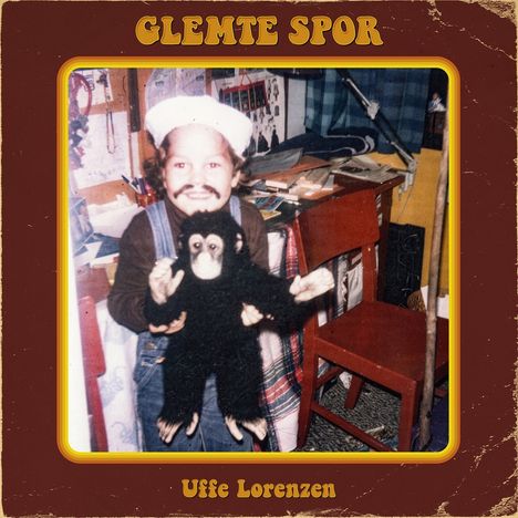 "GLEMTE SPOR" und "Uffe Lorenzen", zeigt ein Kind mit Mütze, das einen Plüschaffen hält, umgeben von Möbeln und Spielzeug.