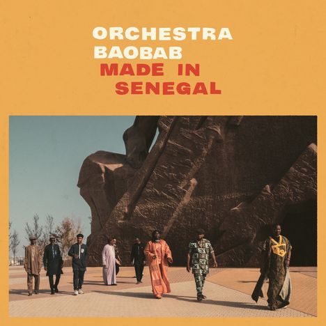 Text: "ORCHESTRA BAOBAB MADE IN SENEGAL". Sieben Menschen gehen vor einer großen Skulptur, blauem Himmel.