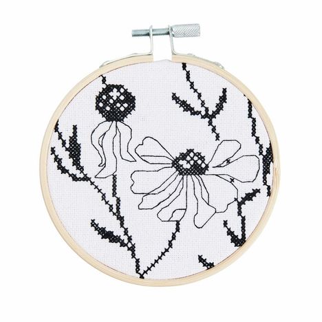 Stickarbeiten in einem Holzrahmen; schwarze Fäden formen Blumenmuster auf weißem Stoff.