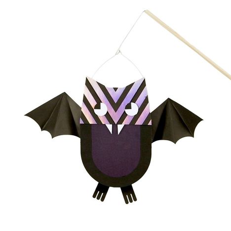Zwei dreieckige Augen, gezackter Mund. Illustration einer Fledermaus aus Papier, violett und schwarz, mit Stab oben.