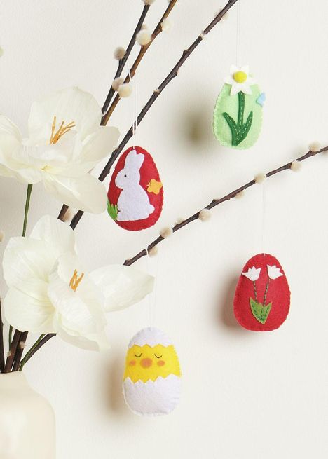 Filzeier mit Hase, Blume, Küken und Tulpen hängen an Ästen mit weißen Blüten.