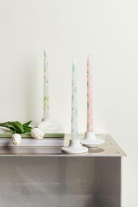 Drei Kerzen mit floralen Mustern in Weiß-, Grün- und Rosatönen stehen auf einem Tisch neben weißen Tulpen.