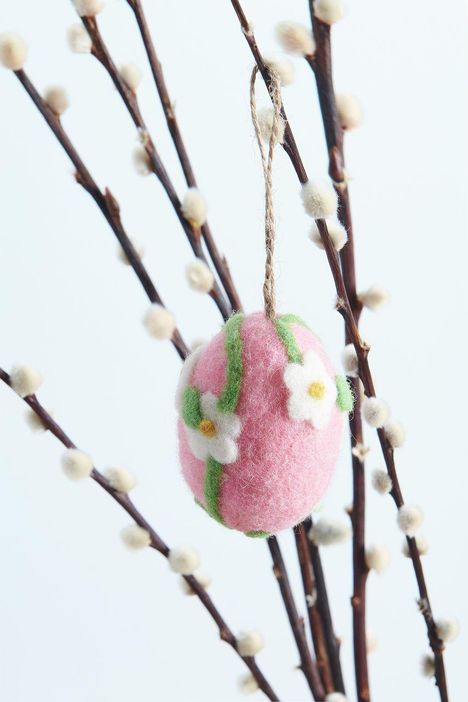 Ein dekoratives, pinkes Filzei mit weißen Blumen hängt an Ästen mit flauschigen Knospen.