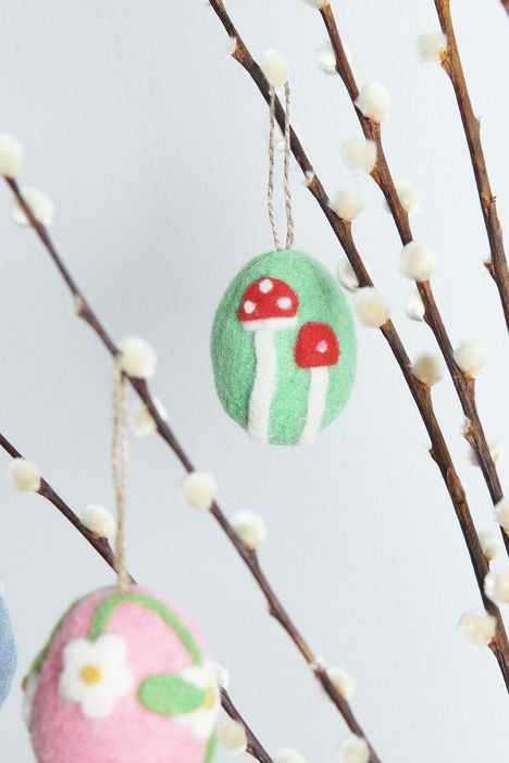 Zwei bemalte Ostereier hängen an Zweigen. Eines hat rote Pilze auf grünem Grund, das andere weiße Blumen auf rosa Grund.