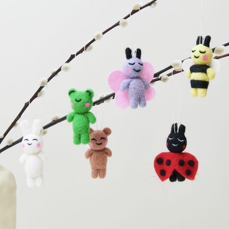 Filzfiguren hängen an einem Ast: Ein Hase, Bär, Marienkäfer, Schmetterling, Biene und Frosch, jeweils mit rosigen Wangen.