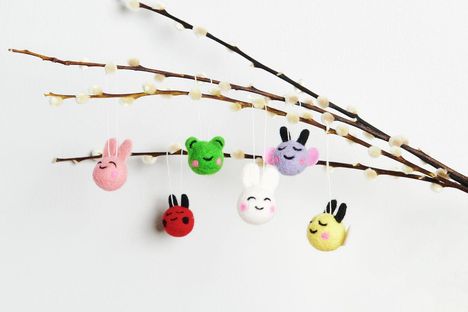 Filzdekorationen in Tierform hängen an Zweigen mit flauschigen Knospen.