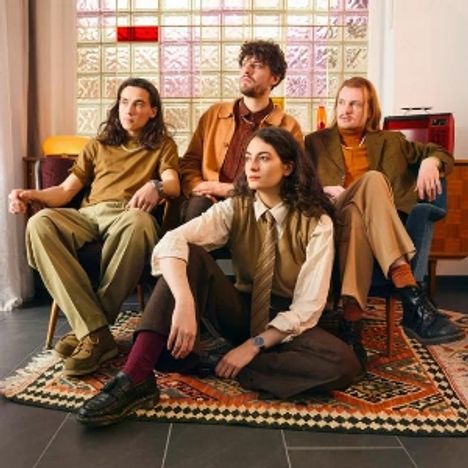 Vier Personen in Retro-Kleidung sitzen und posieren in einem stilvollen, vintage eingerichteten Raum mit Teppich.