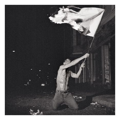 Ein Mann kniet auf der Straße und schwenkt eine brennende Fahne bei Nacht.