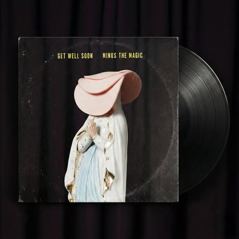 Text: „GET WELL SOON MINUS THE MAGIC“. Abbildung einer Statue mit übergroßem Hut, vor schwarzem Hintergrund.