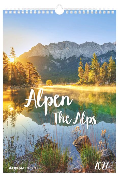„Alpen The Alps 2027“. Ein See mit spiegelndem Wasser, umgeben von Bäumen und Bergen beim Sonnenaufgang.