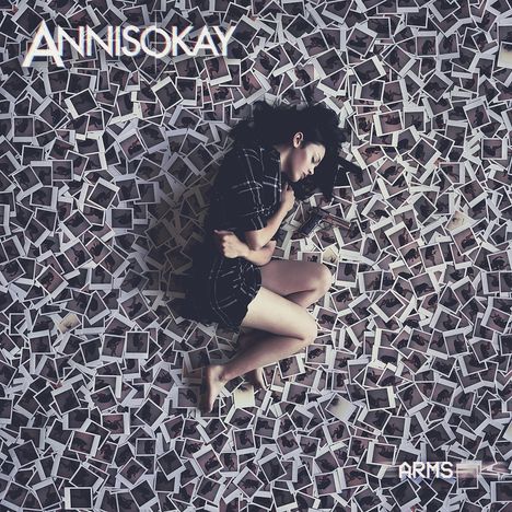 "ANNISOKAY", "ARMS". Frau in Schwarz-Weiß-Kleidung schläft auf einem Bett aus Polaroid-Fotos.