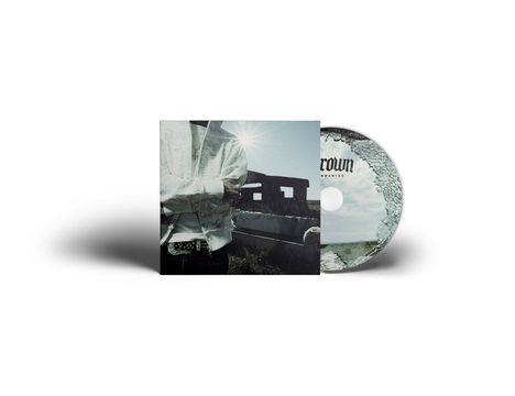 Auf der CD steht "Crown Unwanted". Ein Mann in einer Jacke steht vor einem Gebäude, Sonnenstrahlen scheinen.