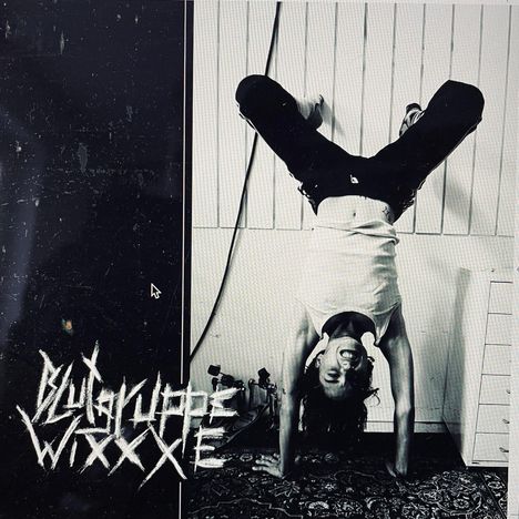 "Blutgruppe WxxxE" in kratziger Schrift. Person in Handstand, lächelt, trägt Tanktop, im Raum mit vertikalen Paneelen.