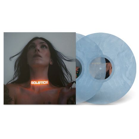 "Solstice" leuchtet auf Hals tätowierter Frau mit wehendem Haar. Zwei hellblaue Schallplatten daneben.