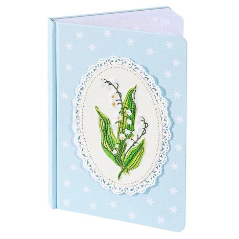 Ein hellblaues Notizbuch mit gesticktem Maiglöckchenmotiv in ovalem weißen Rahmen und weißen Sternen.