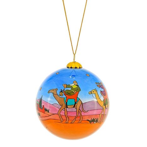 Eine bemalte Weihnachtskugel mit Kamelreitern in einer Wüstenlandschaft vor einem blauen Himmel.