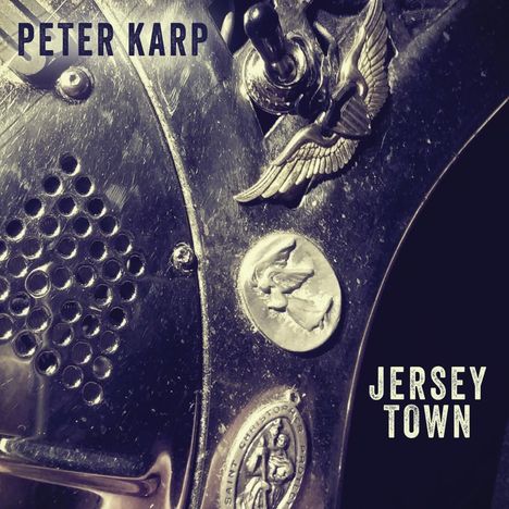 "PETER KARP" und "JERSEY TOWN" in Großbuchstaben auf metallischer Oberfläche mit Emblemen und einem Zugschalter.