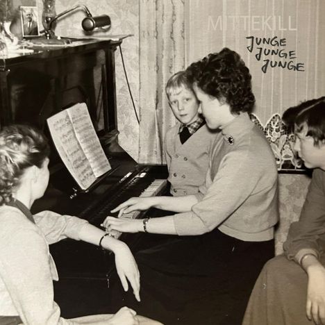 Text: "MITTEKILL" und "JUNGE JUNGE JUNGE". Vier Personen an einem Klavier, eine spielt, andere schauen zu. Schwarz-Weiß.