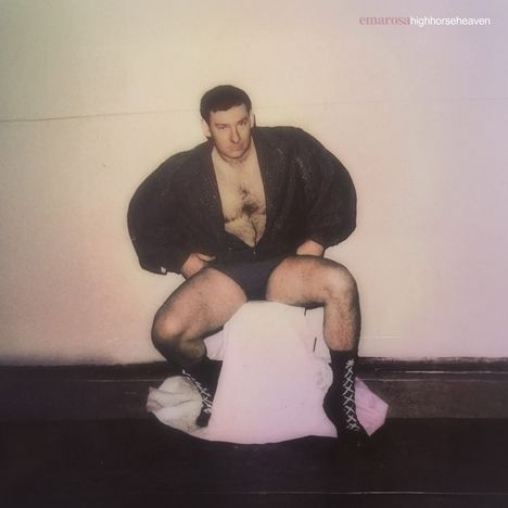 Text: „emarosa highhorseheaven“. Ein Mann sitzt breitbeinig auf einem Stuhl, trägt eine Jacke und Stiefel.