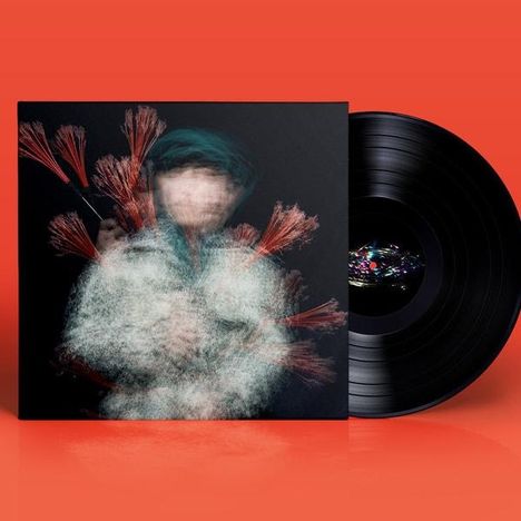 Ein schwarzes Vinyl auf orangefarbenem Hintergrund. Dazu ein unscharfes, abstraktes Cover mit roten Pinselstrichen.
