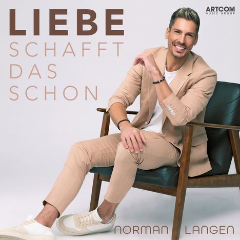 „LIEBE SCHAFFT DAS SCHON“ und „NORMAN LANGEN“. Ein lächelnder Mann in einem beigen Anzug sitzt leger auf einem Stuhl.