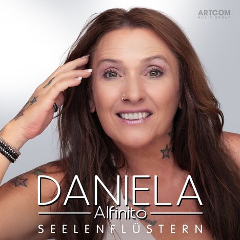 "DANIELA Alfinito SEELENFLÜSTERN" steht über einem lächelnden Gesicht einer Frau mit langen Haaren und Stern-Tätowierungen.